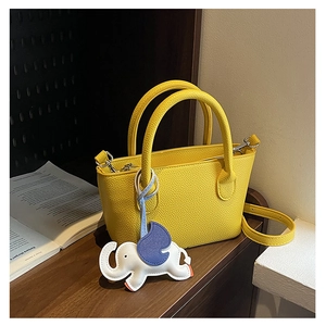 Detail of bright yellow pebbled leather bucket bag featuring a cute white elephant charm
