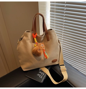 Detail of canvas tote with brown leather handles and a plush bear charm on a seat