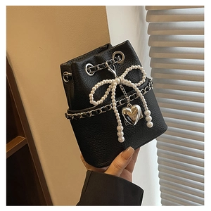 Detail of black pebbled leather bucket bag with pearl bow and silver heart pendant