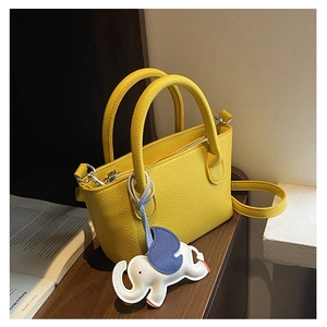 Detail of yellow lychee grain leather handbag featuring elephant charm on wooden table