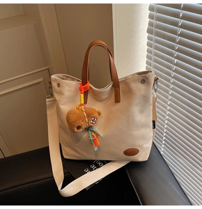 Detail of canvas tote bag with brown leather handles and cute bear charm on sofa