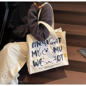 Close-up of off-white canvas tote bag featuring cute cartoon dog and purple artistic lettering