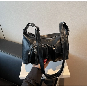 Detailed macro view of black glossy leather shoulder bag with functional utility pockets
