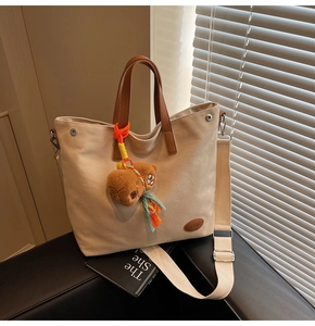 Detail of beige canvas tote bag with leather handles and cute brown bear pendant charm