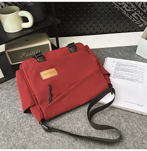 Close-up of red messenger bag with dual plastic buckle closure on grey felt surface