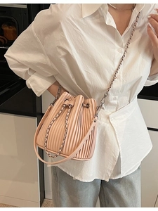 Elegant pleated bucket bag in beige PU leather with silver chain strap shown on model