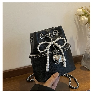 Detail of black pebbled leather bucket bag with pearl bow and silver heart pendant