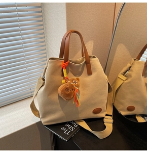 Close-up of beige canvas tote bag with brown leather handles and teddy bear pendant