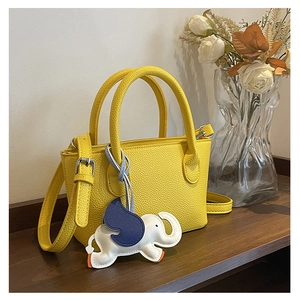 Detail of yellow lychee leather handbag with a blue and white elephant charm accessory