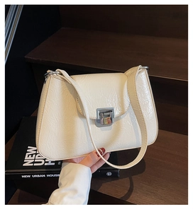 Close-up of cream pleated shoulder bag featuring a modern silver metal lock closure