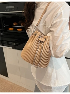 Chic pleated cream bucket bag with drawstring and chain strap shown in a lifestyle setting