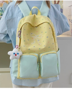 Model wearing yellow plaid backpack with green straps and white bow embroidery detail