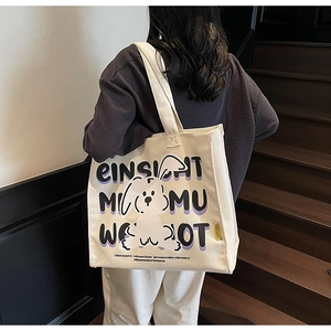 Lifestyle view of woman carrying a large off-white canvas tote with rabbit graphics