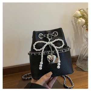 Detail of black lychee leather bucket bag with large pearl bow and silver heart pendant