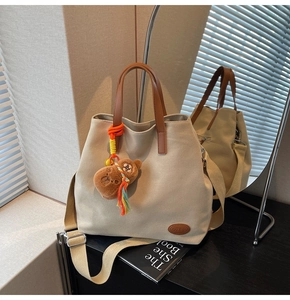 Detail of beige canvas tote bag featuring brown leather handles and a cute plush bear charm