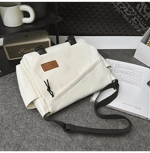 Detailed view of a white canvas messenger bag with black buckles on a minimalist desk