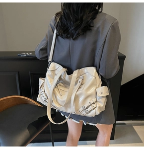 Detail of a large cream tote bag featuring silver zippers, buckles and rivets