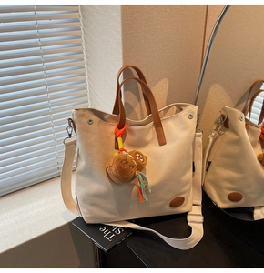 Detail of canvas tote bag with brown leather handles and a cute plush bear charm