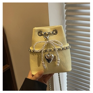 Close-up of cream mini bucket bag featuring pearl bow and silver heart pendant detail