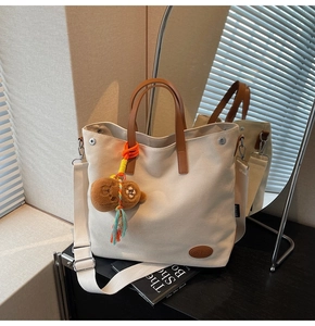 Detail of off-white canvas tote bag featuring brown leather handles and a cute bear charm
