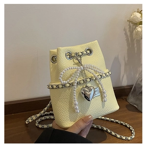 Detail of cream yellow bucket bag with pearl bow, heart charm and lychee texture