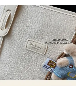 Detailed macro view of cream pebbled leather texture and bear charm on tote bag
