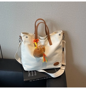 Detail of canvas tote bag with brown leather handles and cute plush capybara charm