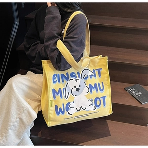 Detail of yellow canvas tote bag featuring cute cartoon dog print and artistic lettering
