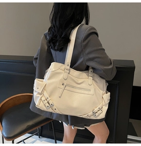 Detail of a large cream-white pleated tote bag with stylish buckles worn by a model