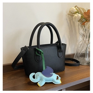 Close-up of black lychee leather bucket bag with cute blue elephant charm on wooden shelf