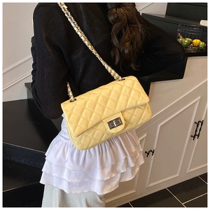 Yellow quilted leather bag detail with silver metal twist lock and chain strap on model