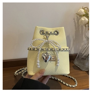 Detail of light yellow lychee grain leather bucket bag with pearl bow and heart charm