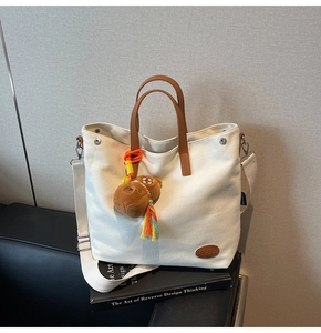 Detail of canvas tote bag with brown leather handles and a cute plush bear charm