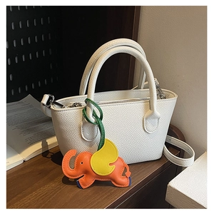 Detail of white lychee leather handbag with cute orange elephant charm and silver hardware
