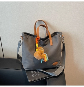Detail of grey canvas tote bag with brown leather handles and a horse plush charm