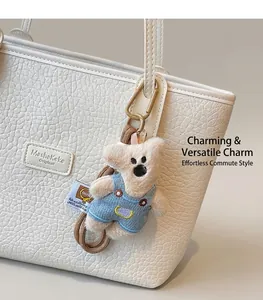Detail of cute plush bear charm in denim overalls on a textured white leather tote bag