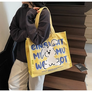 Close-up of yellow canvas tote bag with rabbit illustration worn on shoulder by model