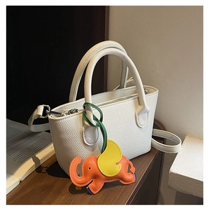 Close-up of white lychee leather bucket bag featuring a vibrant elephant charm detail