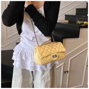 Detail of light yellow quilted crossbody bag with metal chain strap worn by a model