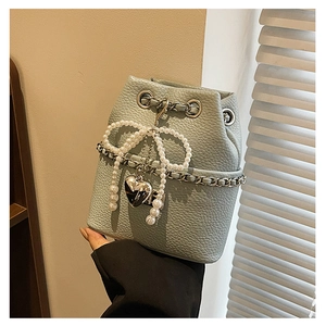 Close-up of light blue bucket bag featuring pearl bow and heart charm on chain strap