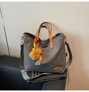 Close-up of grey canvas tote bag with leather handles and cute bear plush charm