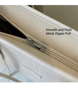 Detail view of smooth metal zipper head on white lychee grain leather tote bag