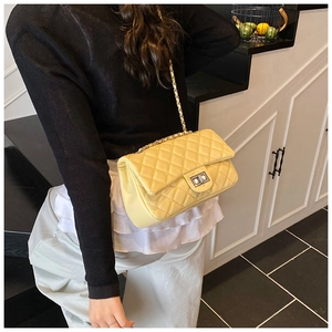 Model wearing a bright yellow quilted crossbody bag with silver twist lock and chain strap