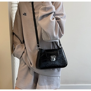 Détail d'un sac à bandoulière en cuir gaufré noir avec fermoir argenté sur un ensemble