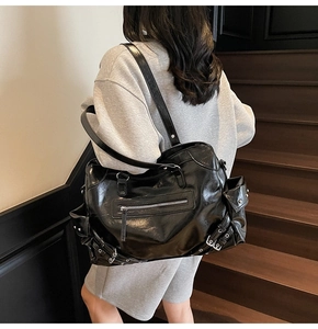 Detail of a large black moto-style tote bag with functional pockets on a female model