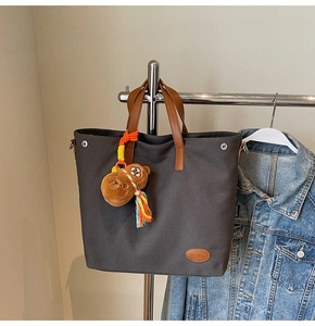 Detail of charcoal grey canvas tote bag with brown leather handles and a plush bear charm