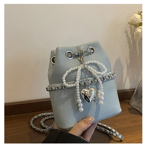 Close-up of light blue bucket bag featuring pearl bow and silver heart pendant detail