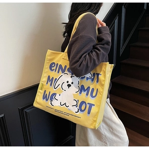 Detail view of a yellow canvas tote bag with cartoon dog print on model's shoulder