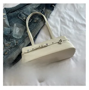 Close-up of cream underarm bag with silver metal lock and belt detail on white fabric