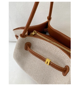 Close-up of contrast canvas tote bag with brown leather trim and golden zipper detail